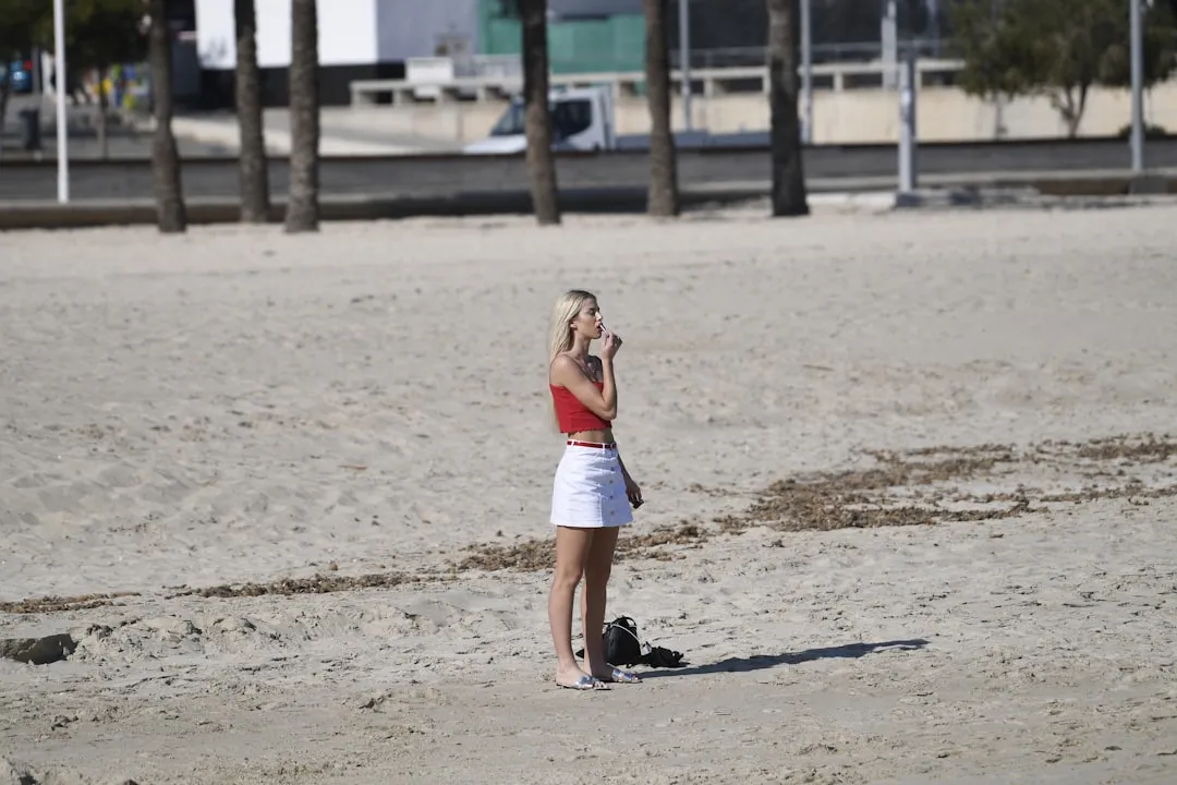 Woman in red top and white skirt on sandy beach.