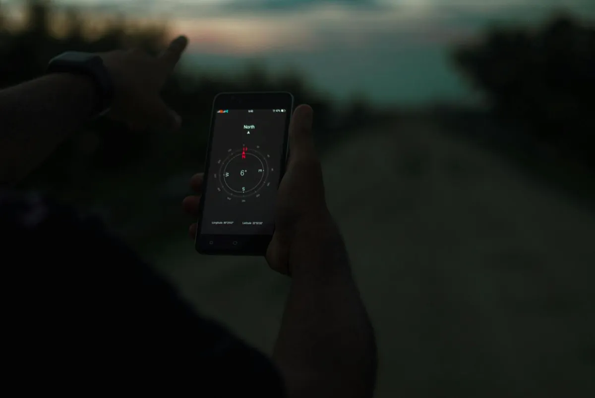 Person navigating using a smartphone compass app outdoors at twilight.