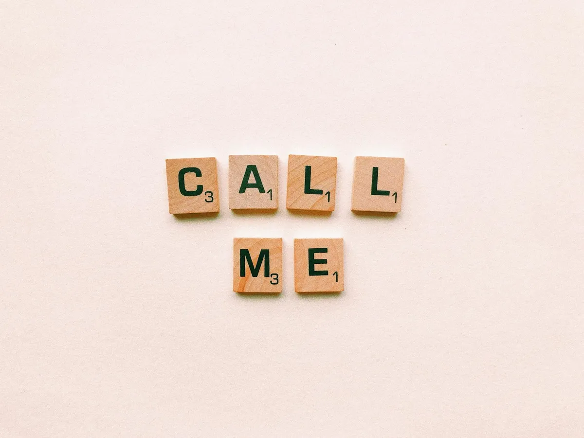 Wooden letter tiles spelling 'Call Me' on a pastel pink background, invoking communication and connection.